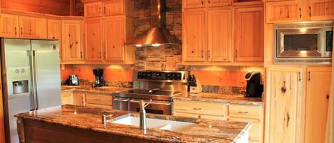 A kitchen with wooden cabinets, a granite countertop, stainless steel appliances, and a stone accent wall.