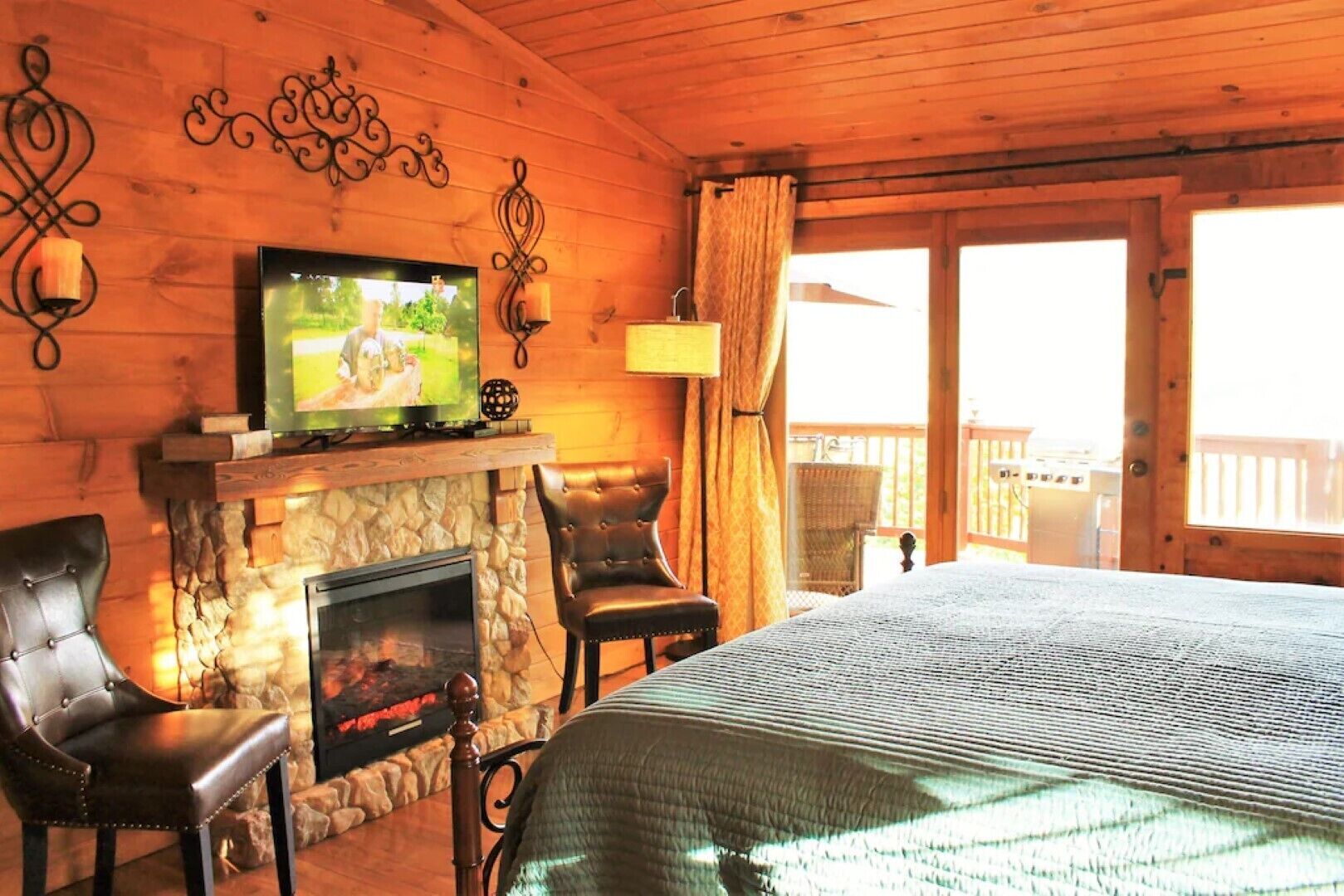 A cozy cabin room with a stone fireplace, a television, leather chairs, and a large bed.