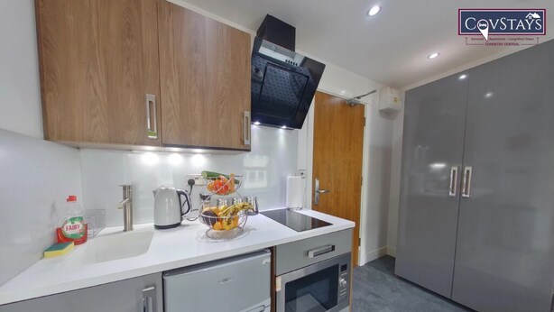 A modern kitchen with stainless steel appliances, wooden cabinets, and a grey wardrobe. - Victoria House - Deluxe Studio by CovStays (Coventry)