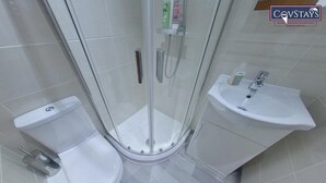 A bathroom with a glass-enclosed shower, a toilet, and a sink. - Victoria House - Deluxe Studio by CovStays (Coventry)