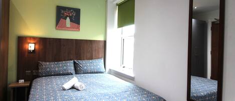 Una habitación de hotel con una cama, una mesita de noche, un espejo en la pared y una ventana con persianas.