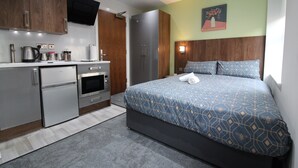 A modern hotel room with a kitchenette, a bed with blue patterned bedding, and a painting on the wall. - Victoria House - Deluxe Studio by CovStays (Coventry)