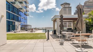 A rooftop terrace with outdoor seating, a pool, and modern buildings in the background.