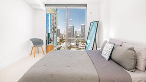 A bedroom with a large bed, a chair, and a view of a cityscape through a sliding door.