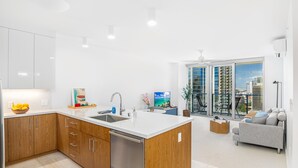 A modern kitchen with a central island, a dining area with a grey sofa, and a large window with a city view.