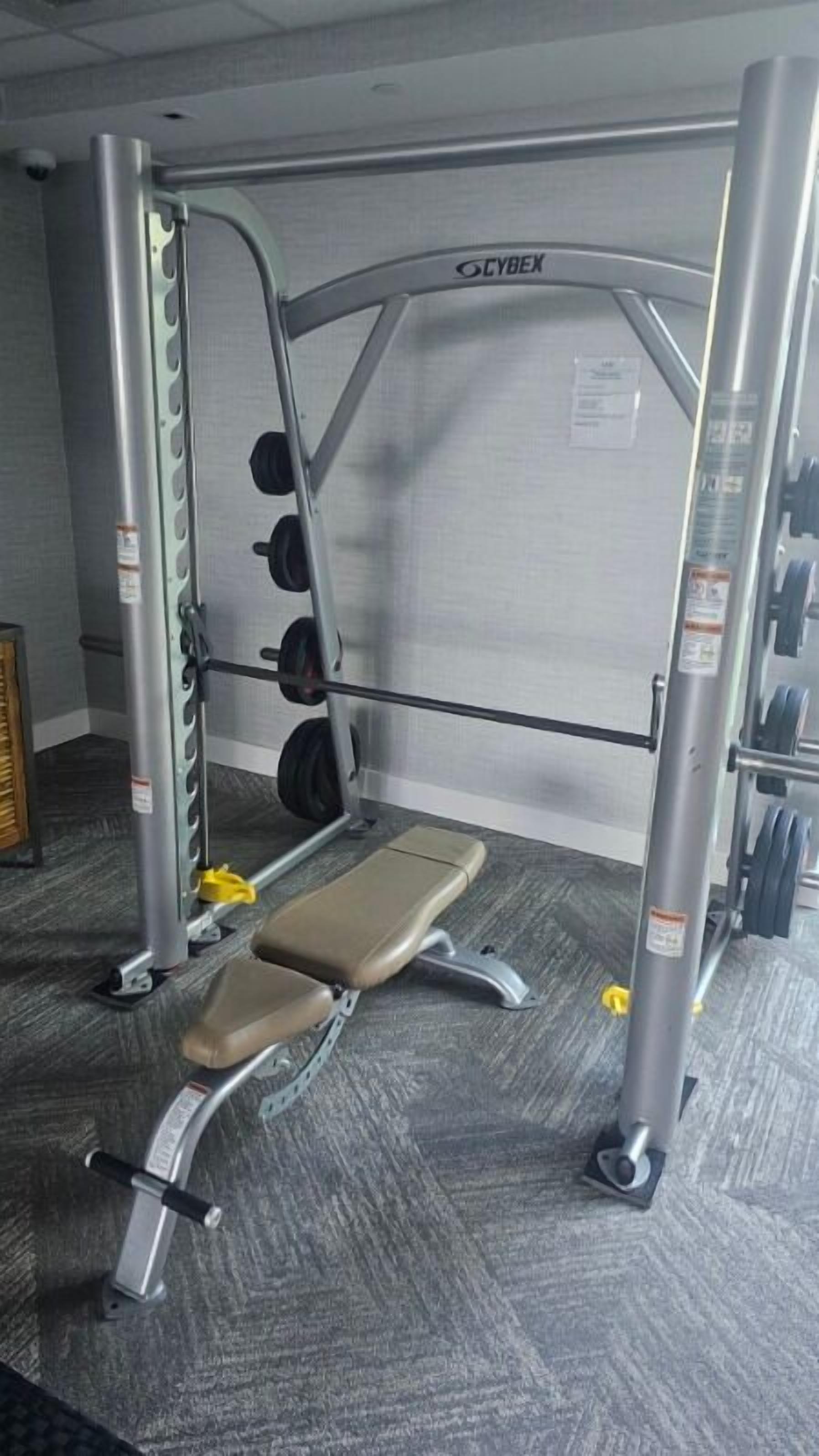 A gym with a Cybex weight bench, weight plates, and a squat rack.