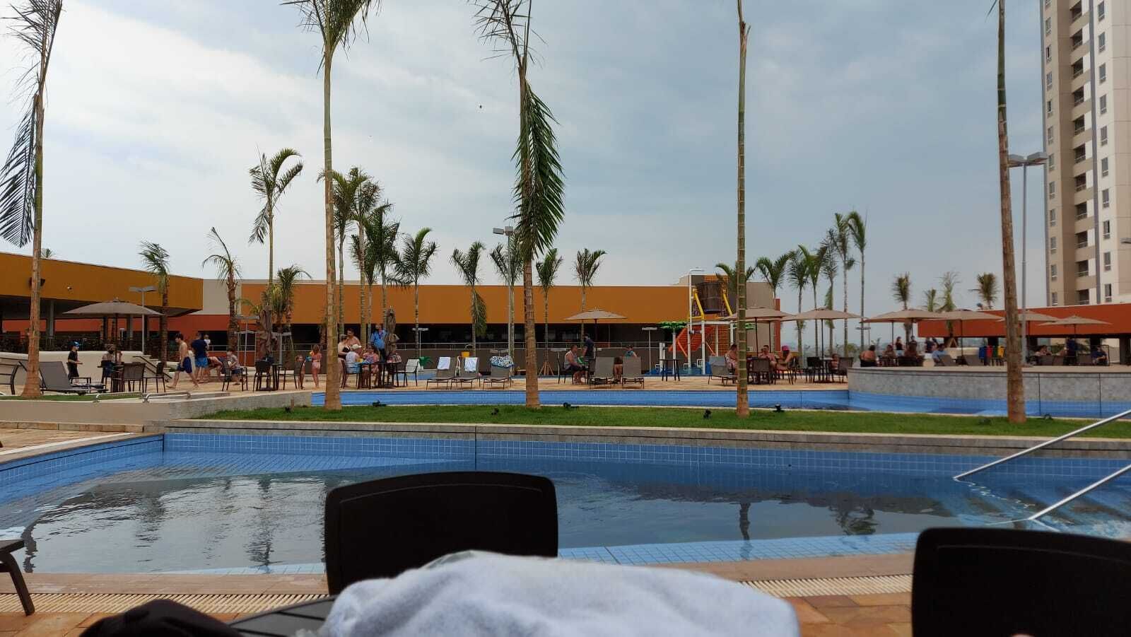 A swimming pool area with lounge chairs, palm trees, and a building in the background.