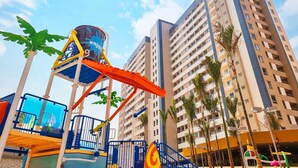 A water park with a blue and orange play structure, surrounded by tall residential buildings and palm trees. - Solar das Águas Park Resort - Olimpia SP (Olímpia)