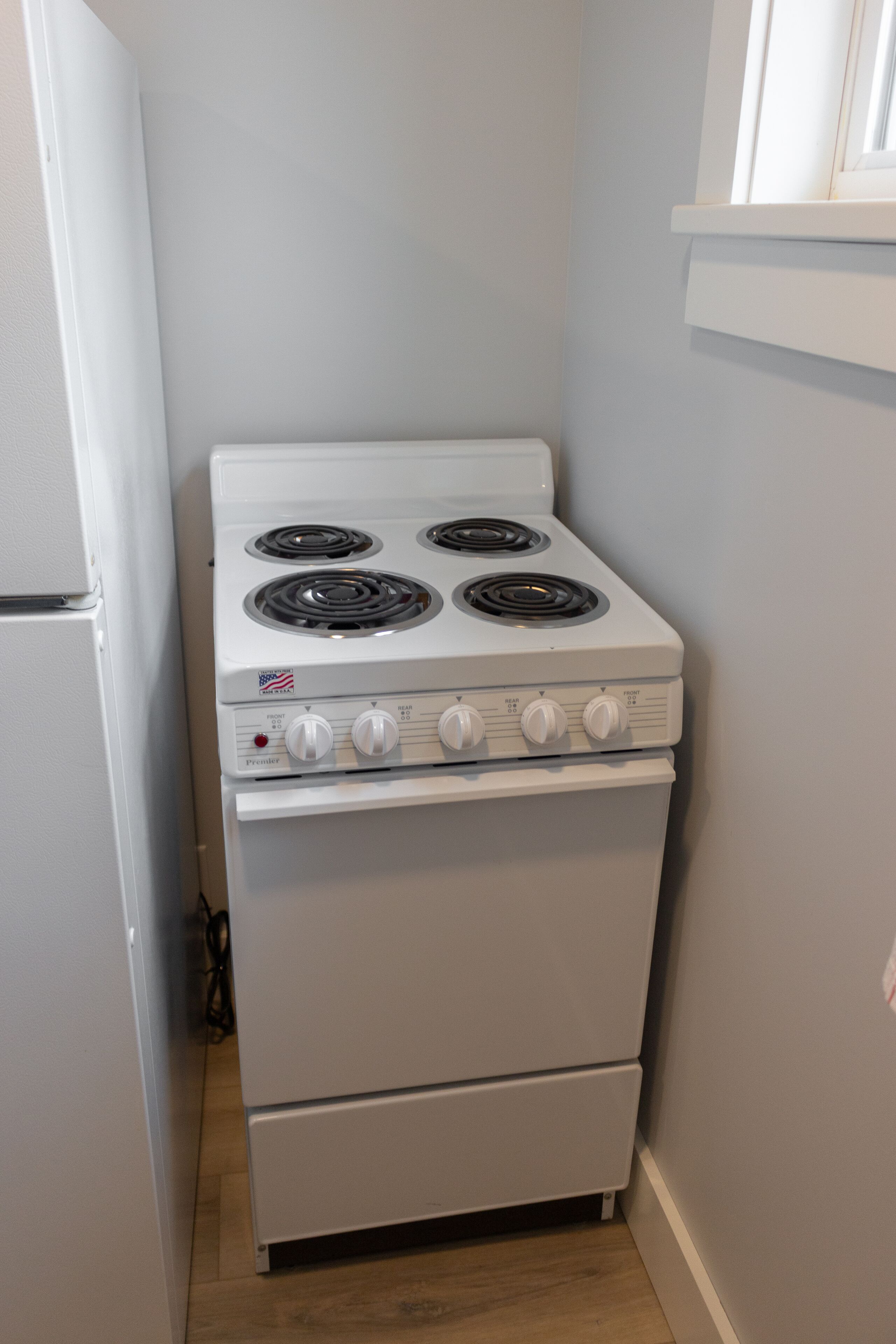 A compact kitchen with a white stove, a refrigerator, and a wooden floor.