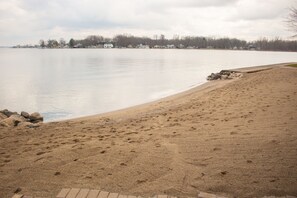 Une plage de sable avec des empreintes, un lac paisible et des maisons en arrière-plan.