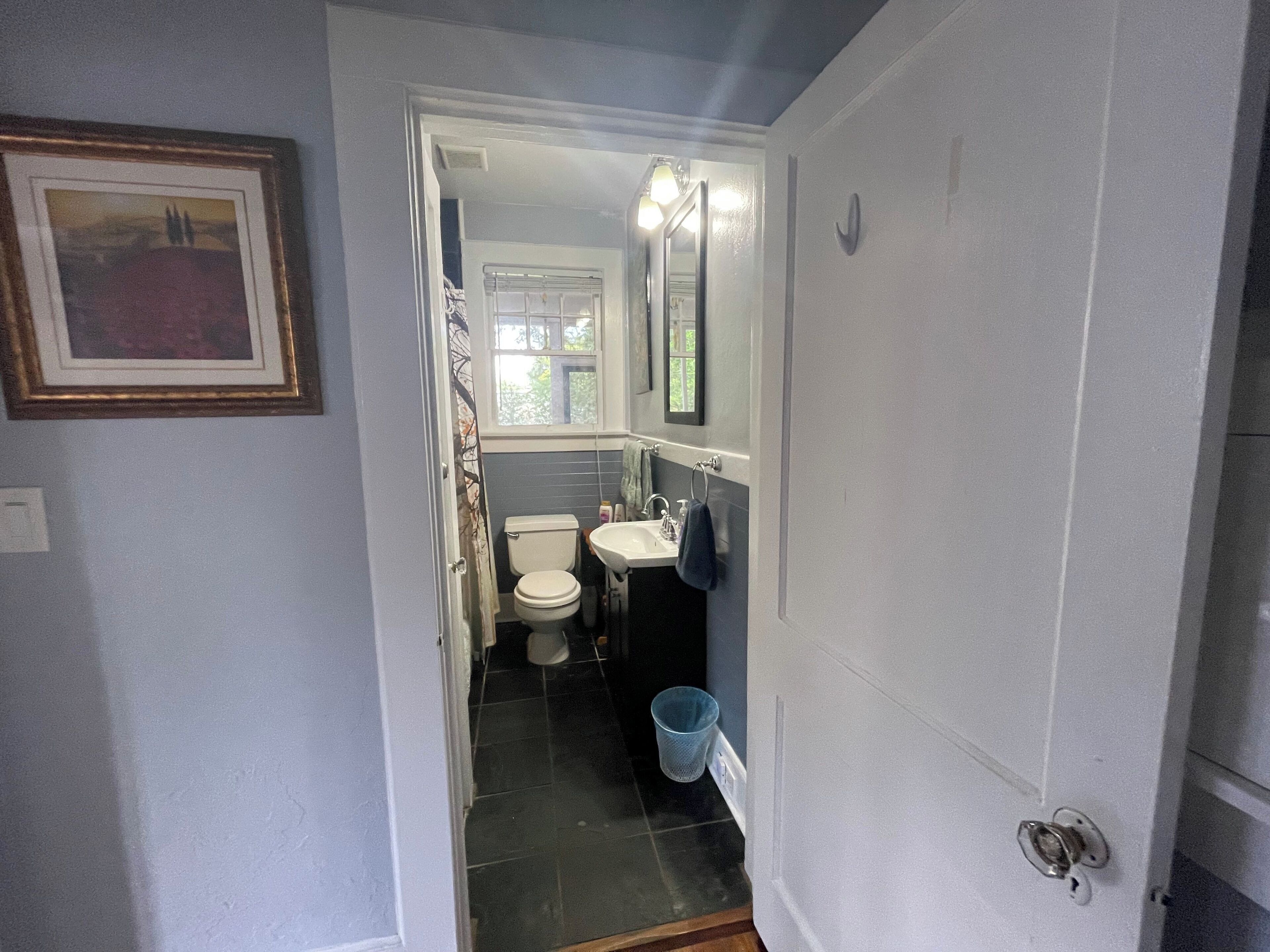 A narrow bathroom with a toilet, sink, and mirror.