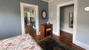 Une chambre avec un lit, un bureau et une chaise. Un couloir mène à une salle de bain et à un coin repas.