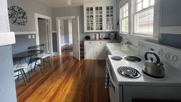 Une cuisine avec un plancher en bois, des armoires blanches, une cuisinière et un ventilateur de plafond.