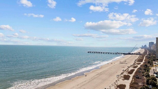 A beach with a pier extending into the ocean, a sandy shoreline, and buildings in the background. - The Pink Flamingo | Bold & Vibrant By The Beach (Myrtle Beach)