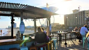 A beachside restaurant with outdoor seating, a menu board, and a view of the beach and ocean. - The Pink Flamingo | Bold & Vibrant By The Beach (Myrtle Beach)