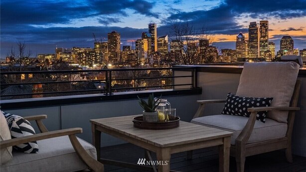 Una terraza en la azotea con vistas al horizonte urbano, amueblada con una silla, una mesa y elementos decorativos.