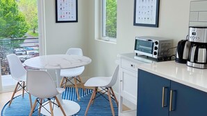 Una cocina moderna con encimera blanca, una cafetera, un tostador y un menú de café enmarcado en la pared.