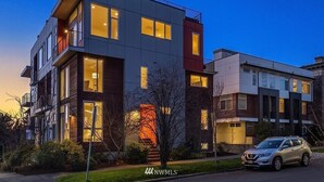 Un edificio residencial moderno de varios pisos con grandes ventanales y balcones, una escalera visible y un coche estacionado.