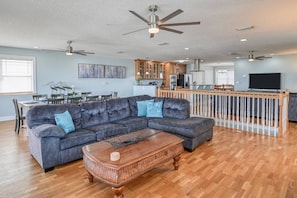 A spacious living room with a dark gray sectional sofa, a wooden coffee table, and a dining area with a white table and chairs. - Atlantic Blue (St. Augustine)