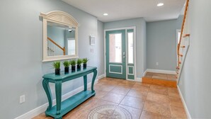A hallway with a teal console table, a mirror, and a door with a green frame. - Atlantic Blue (St. Augustine)