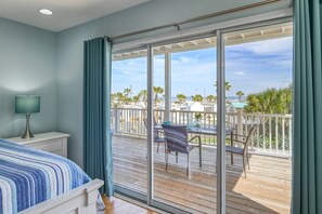 A bedroom with a large sliding glass door leading to a balcony with a view of the beach and palm trees. - Atlantic Blue (St. Augustine)