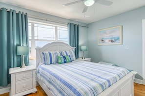 A bedroom with a bed, two bedside tables, a ceiling fan, a window with curtains, and a painting on the wall.