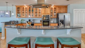 A kitchen with a central island, wooden cabinets, stainless steel appliances, and a light blue wall. - Atlantic Blue (St. Augustine)