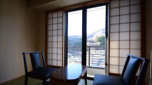 Una habitación tradicional japonesa con suelo de tatami, una mesa de madera baja y dos sillas oscuras.