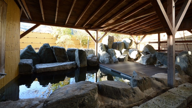 Un espacio al aire libre cubierto con una terraza de madera, rocas grandes y un pequeño estanque.