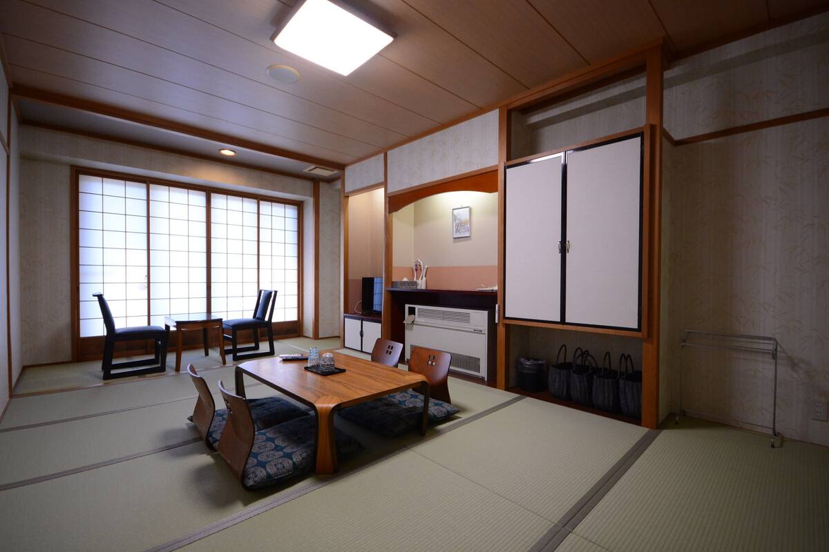 Una habitación japonesa tradicional con suelo de tatami, una mesa baja con cojines y puertas correderas.