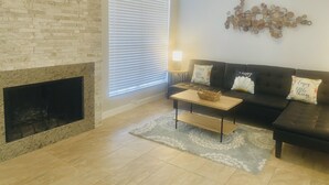 Un salon avec une cheminée en pierre, un canapé foncé, une table basse et un élément décoratif mural.
