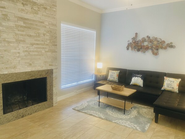 Ein Wohnzimmer mit Kamin aus Stein, einem dunklen Sofa, einem Couchtisch und einem Wandbild.