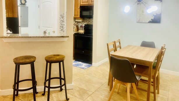 Un coin repas avec une table et des chaises en bois, une cuisine avec des meubles et des appareils électroménagers en bois, et un bar avec des tabourets.