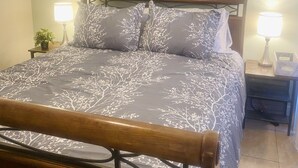Un lit bien fait, recouvert d’une couvre-lit à motifs floraux, deux lampes de chevet, une table de chevet avec une lampe, et un tableau représentant un paysage, accroché au-dessus du lit.