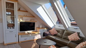 A compact living space with a TV, sofa, and storage cabinets, featuring a sloped ceiling and skylight.