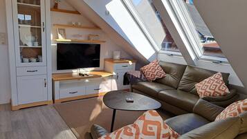 Ein kompakter Wohnbereich mit Fernseher, Sofa und Stauraum, mit schrägverdeckter Decke und Oberlicht.