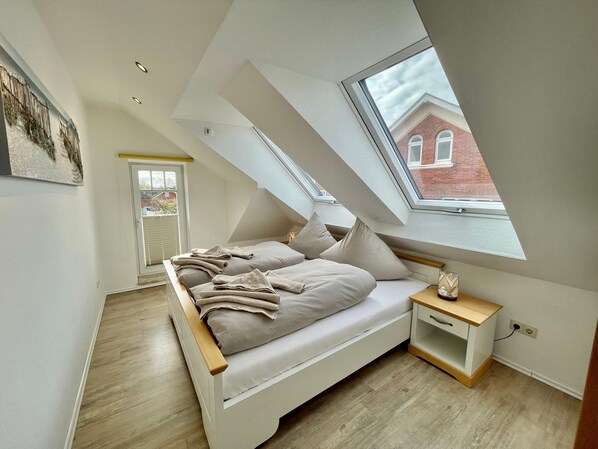 A modern loft bedroom with a sloped ceiling, a skylight, and a view of a brick building.