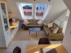 Ein gemütliches Lofts Apartment mit hohen Decken, Oberlichtern, einer Sofagarnitur, einem Couchtisch und einem Essbereich.