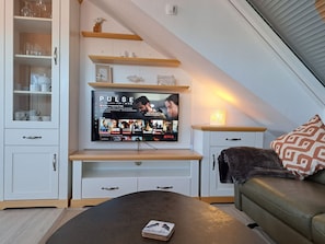 Ein modernes Wohnzimmer mit einem flachbildfernseher an einem Holzbodenregal, einem Ledersofa und einem Couchtisch mit einer Zeitschrift.