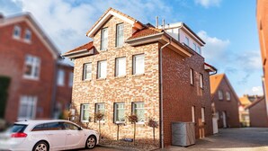 A two-story residential building with a brick facade, multiple windows, and a car parked in front.
