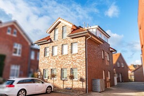 En tvåvånings bostadsbyggnad med en fasad av tegel, flera fönster och en bil parkerad framför.