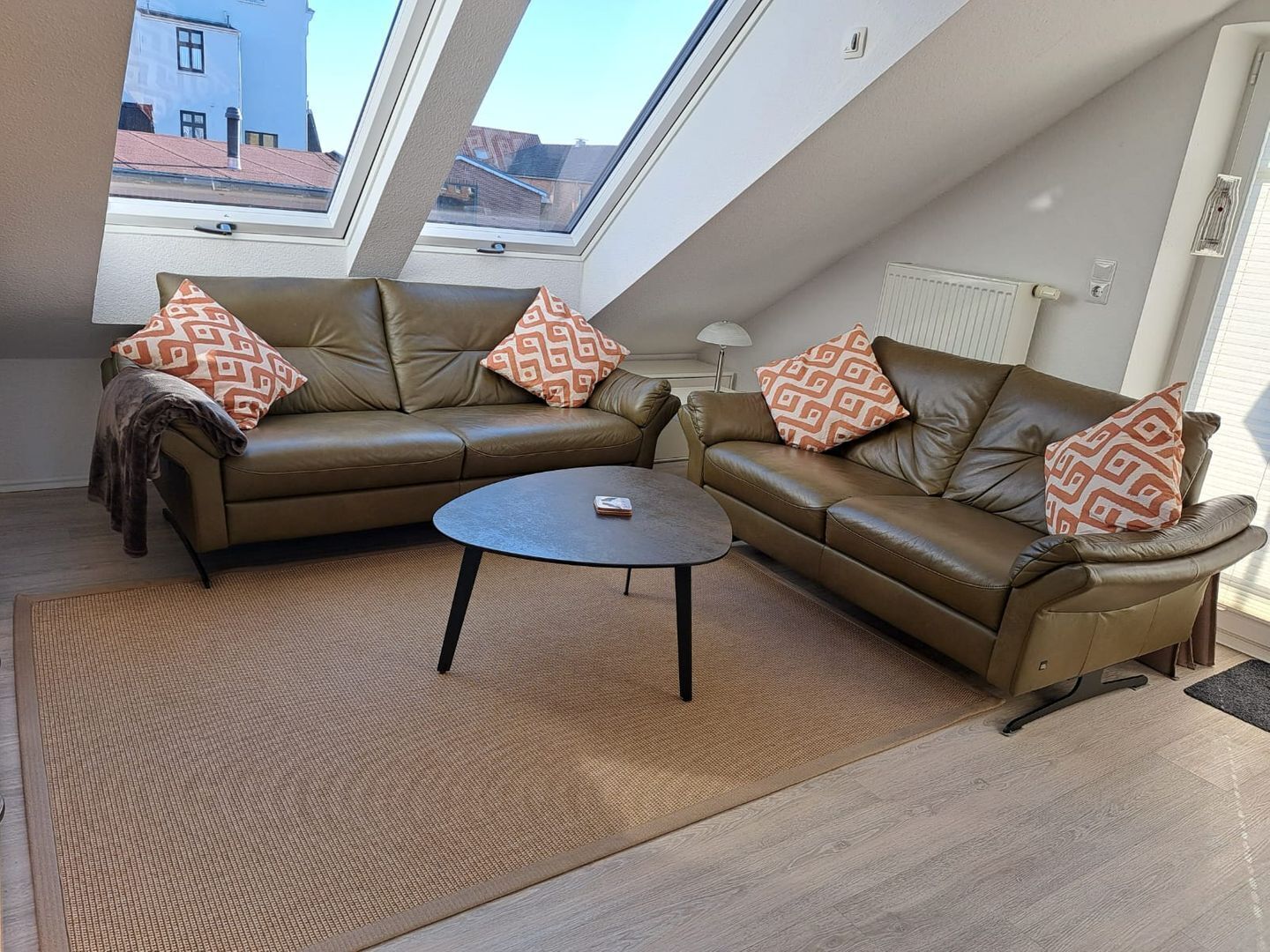 Eine moderne Loft-Wohnung mit einem braunen Ledersofa, einem runden Couchtisch und Kissen mit Muster.