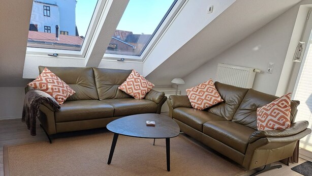 A modern loft apartment with a brown leather sofa set, a round coffee table, and patterned throw pillows.