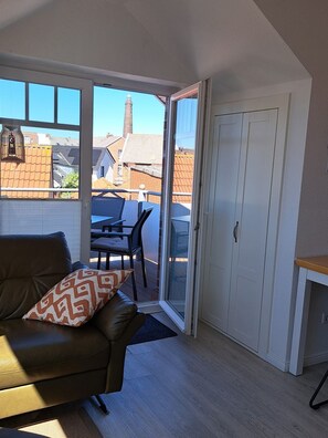 Ein Zimmer mit einer braunen Ledersofa, einem Esstisch mit Stühlen und einer Glastür, die auf eine Terrasse im Freien führt.