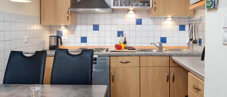 A compact kitchen with wooden cabinets, a stainless steel range hood, and a tiled backsplash.