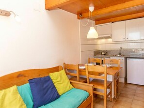 Ein gemütliches Zimmer mit einem hölzernen Bett, einem Esstisch mit Stühlen, einer Küchenzeile inklusive Herd und Spüle sowie einer Pendelleuchte.