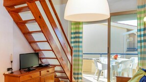 A room with a wooden desk, a television, a sofa, and a balcony with a table and chairs.