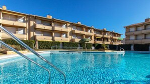 A clear swimming pool with metal railings, surrounded by a building with multiple balconies and a well-maintained hedge.