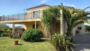 Una casa a due piani con un balcone, circondata da piante diverse e un prato curato.