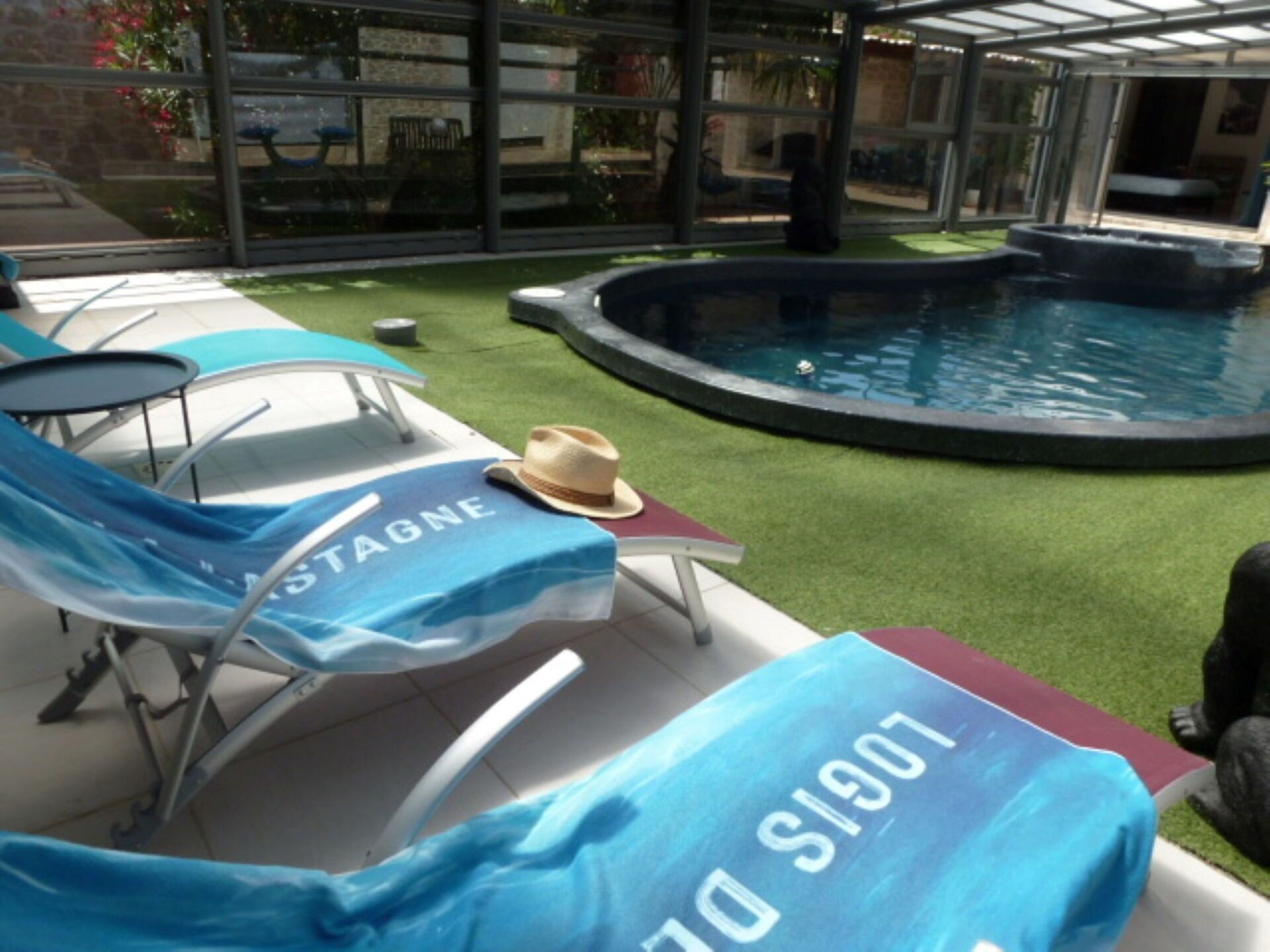 Area piscina con lettini, un cappello su un tavolo e un cartello con del testo.